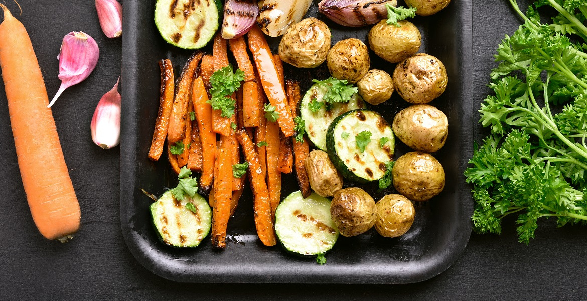 Das Bild zeigt eine Platte mit geröstetem Gemüse - Möhren, Zucchini, junge Kartoffeln, Zwiebeln und Knoblauch
