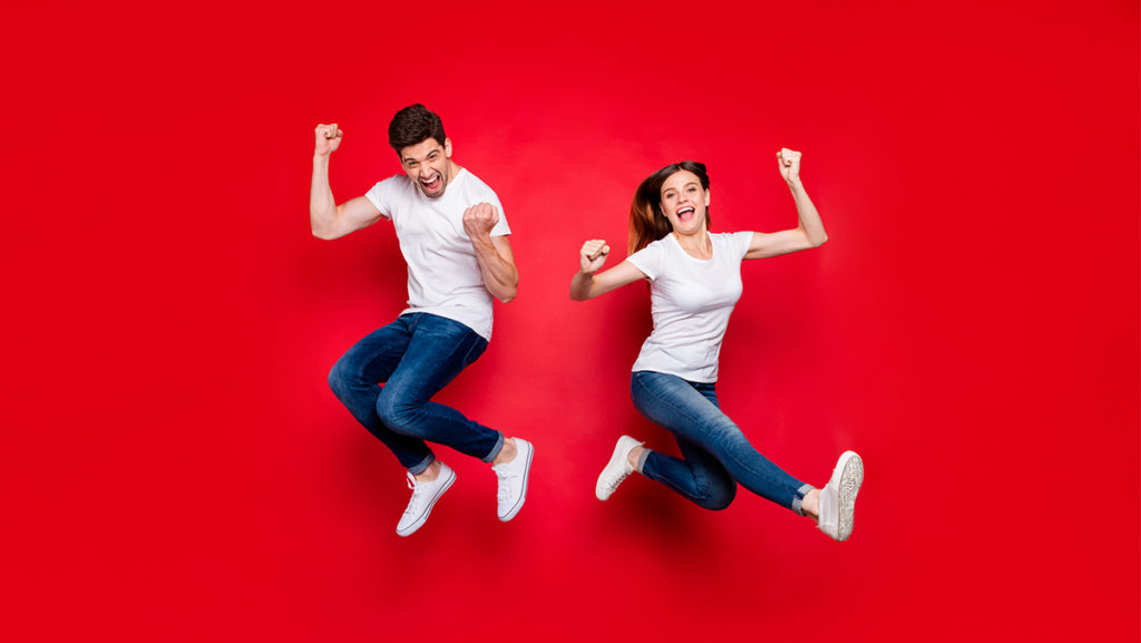 Das Foto zeigt zwei Personen die lachend in die Luft springen
