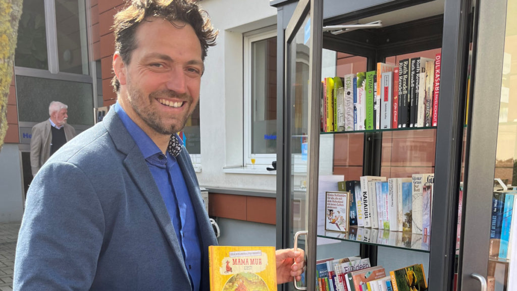 Das Foto zeigt den Bürgermeister von stolberg, Patrick Haas vor dem Bücherschrank des Helene-Weber-Hauses in Stolberg
