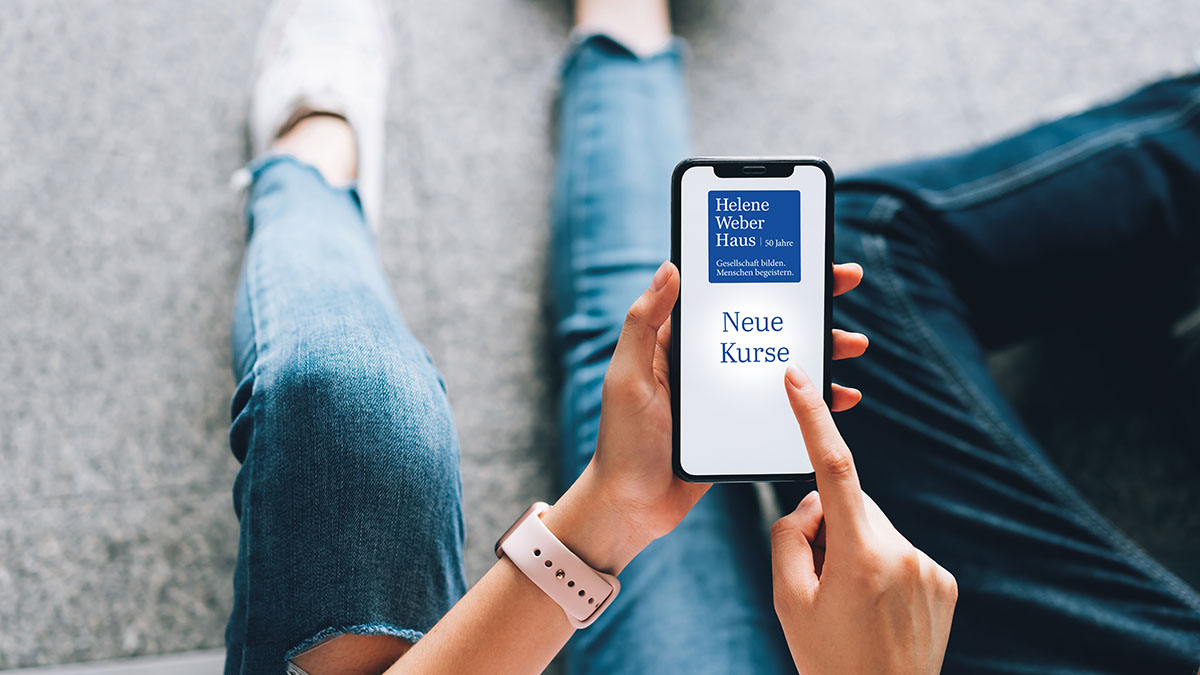 Eine Frau, die ein Smartphone in der Hand hält. Auf dem Smartphone sieht man den Schriftzug Neue Kurse.