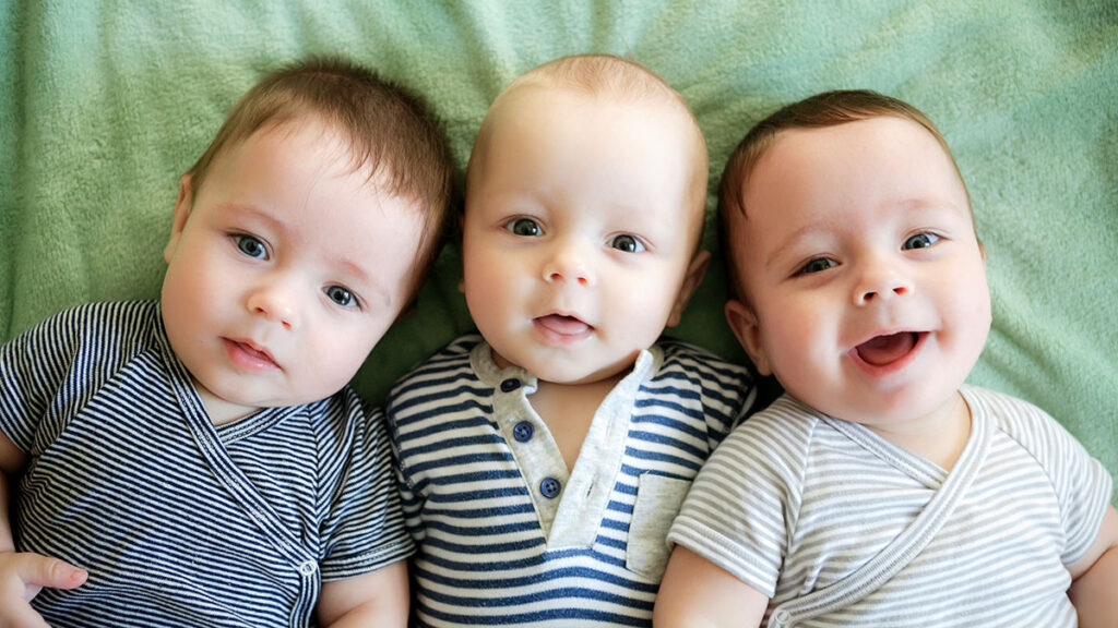 Drei Babys schauen lachend und neugierig in die Kamera