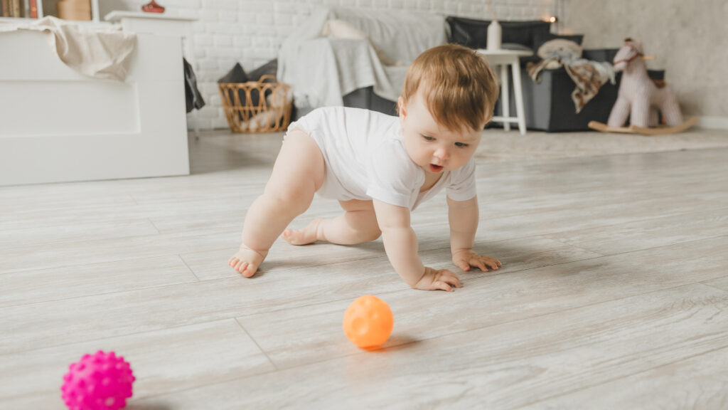 Ein Baby spielt mit einem Gummibal auf dem Boden