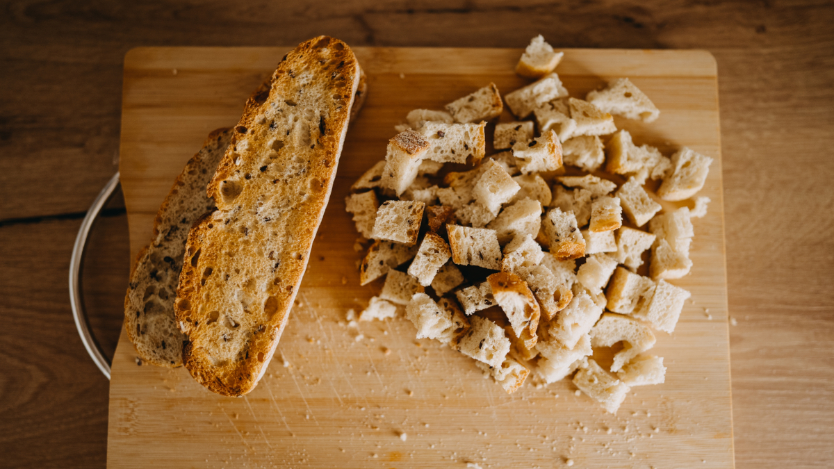 Das Foto zeigt 2 Brotscheiben und in kleiner Würfel geschnittenes Brot auf einem Holschneidebrett.