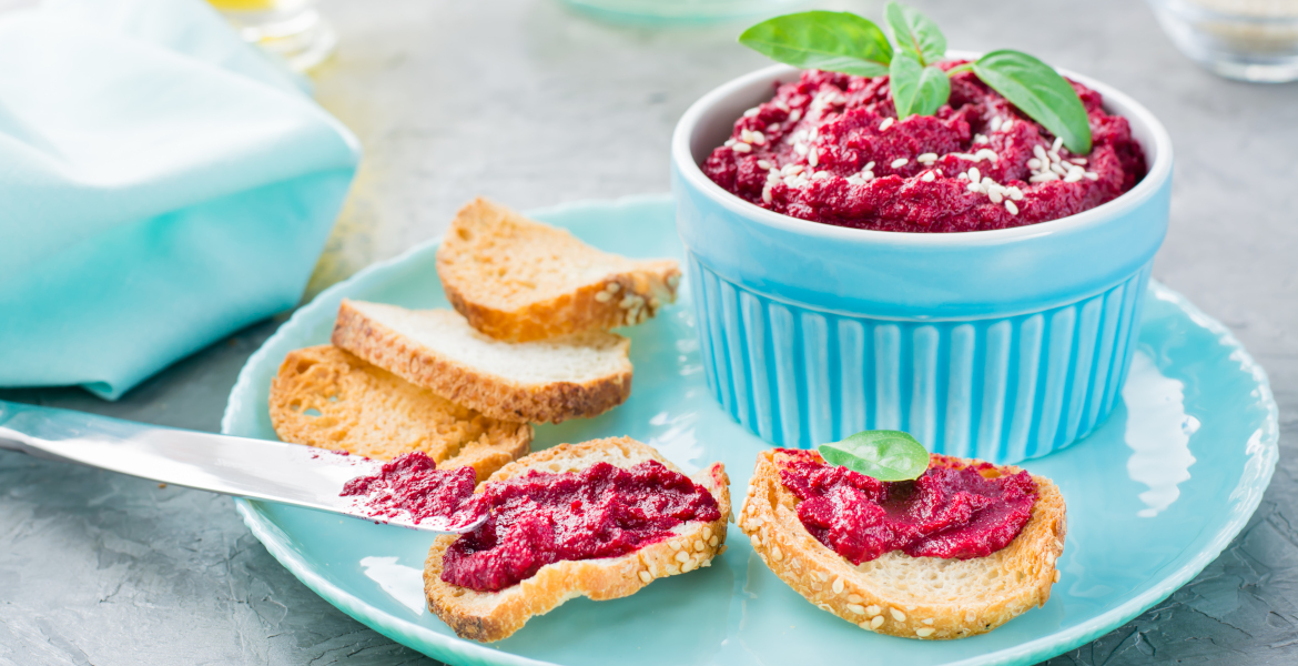 Hausgemachte Bruschetta mit Rote-Bete-Hummus auf kleinem Toast auf einem Teller und einem Tafelmesser auf dem Tisch