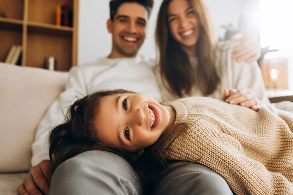 Lächelndes Mädchen im Schoß seiner Eltern auf einer Couch