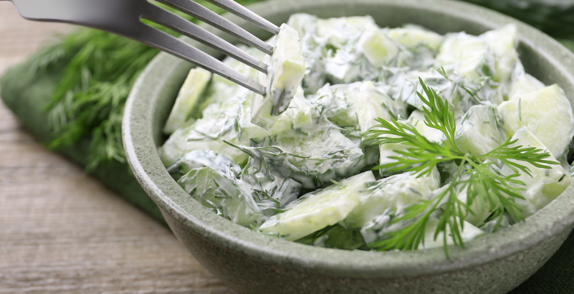 Cremiger Gurkensalat mit Dill, Gurkenscheiben und frischen Kräutern in einer grünen Schale.
